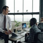 Three men engaged in a business meeting in a modern office setting with laptops and documents. — 5 Tips To Gain Followers On
