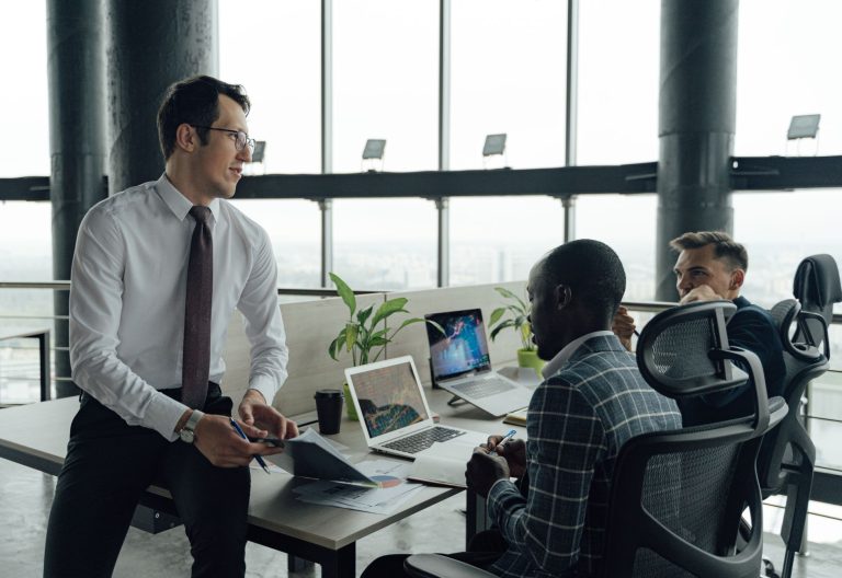 Three men engaged in a business meeting in a modern office setting with laptops and documents. — 5 Tips To Gain Followers On