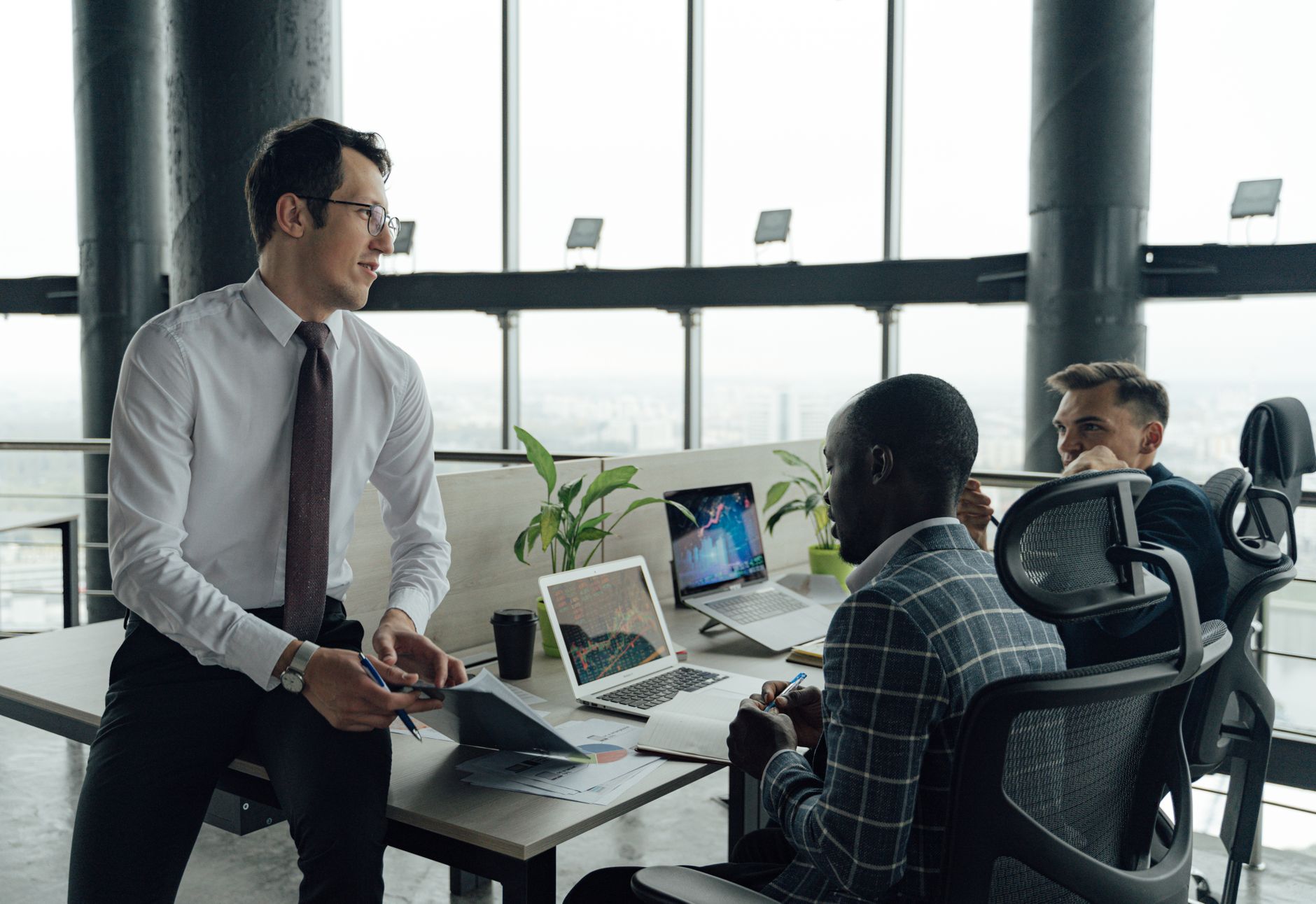 Three men engaged in a business meeting in a modern office setting with laptops and documents. — 5 Tips To Gain Followers On