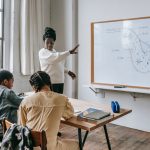 African American female teacher standing near whiteboard and giving lecture to ethnic teenagers during biology lesson — 7 tip