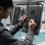 A technician works on a computer motherboard using tools at a workspace, focusing on electronics repair. — 8 Notable Features