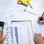 Colleagues collaborating on financial charts and graphs using mobile and paper documents in the office. — Advantages Of CFDs