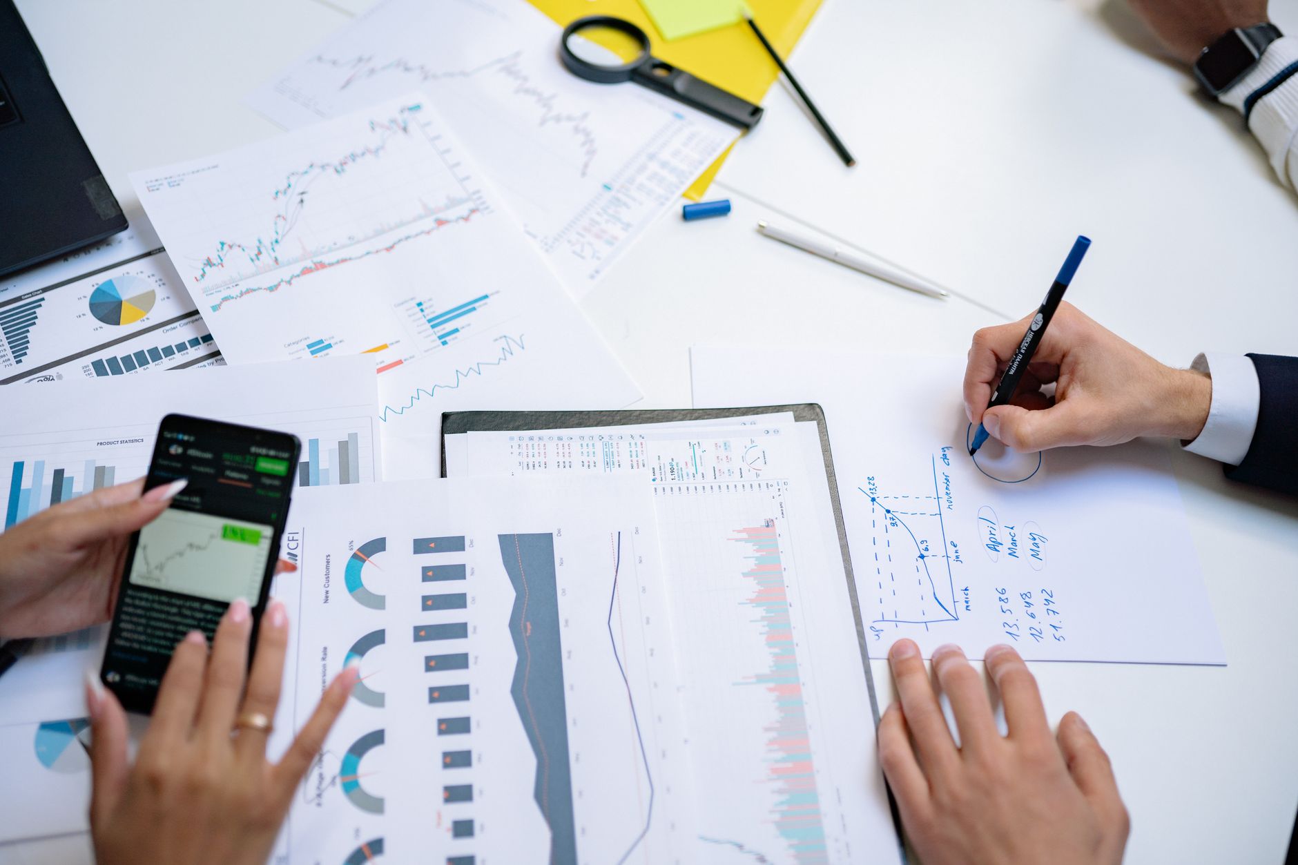 Colleagues collaborating on financial charts and graphs using mobile and paper documents in the office. — Advantages Of CFDs