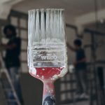Detailed close-up of a paintbrush with men painting a wall in the blurred background, highlighting renovation work. — Advanta