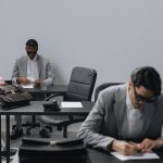 Business office with diverse employees in gray suits working at desks in an indoor setting. — Asbestos Surveys Explained: A S