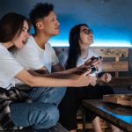 Three friends play video games together indoors, enjoying pizza and fun times. — Avail of a wide variety of perks through gam