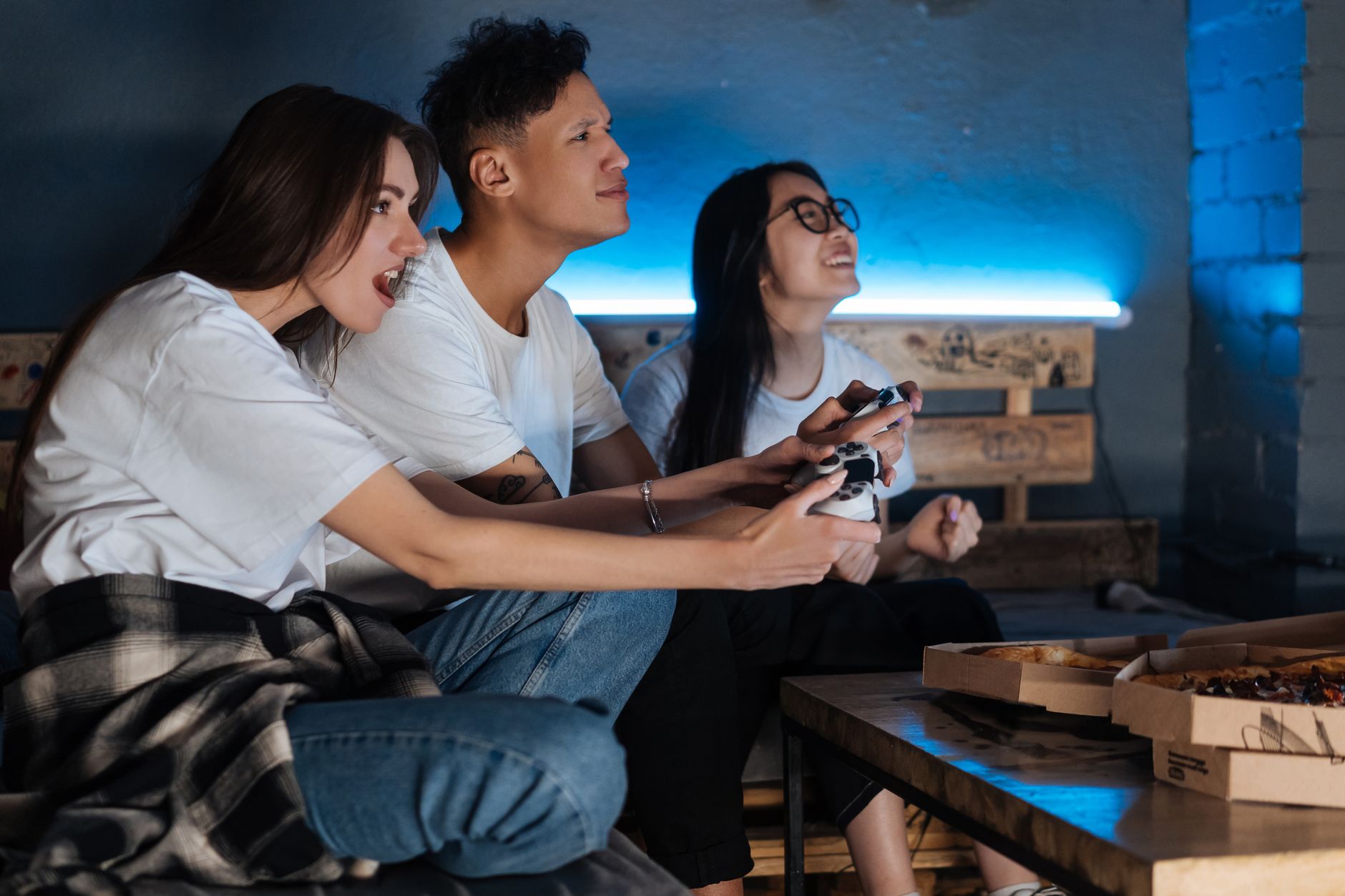 Three friends play video games together indoors, enjoying pizza and fun times. — Avail of a wide variety of perks through gam