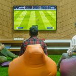 Three friends relaxing and playing a soccer video game indoors on a comfortable game night. — Be Knowledgeable With The Speci