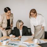 Three businesswomen discussing documents during a meeting in a modern office setting. — Become a Pro Player with These Essent