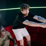 Two young men having fun playing video games in a cozy indoor setting. — Chronicles of Triumph: Lsm99 Casino's Epic Tales of