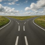 A fork in the road surrounded by green fields under a cloudy sky.