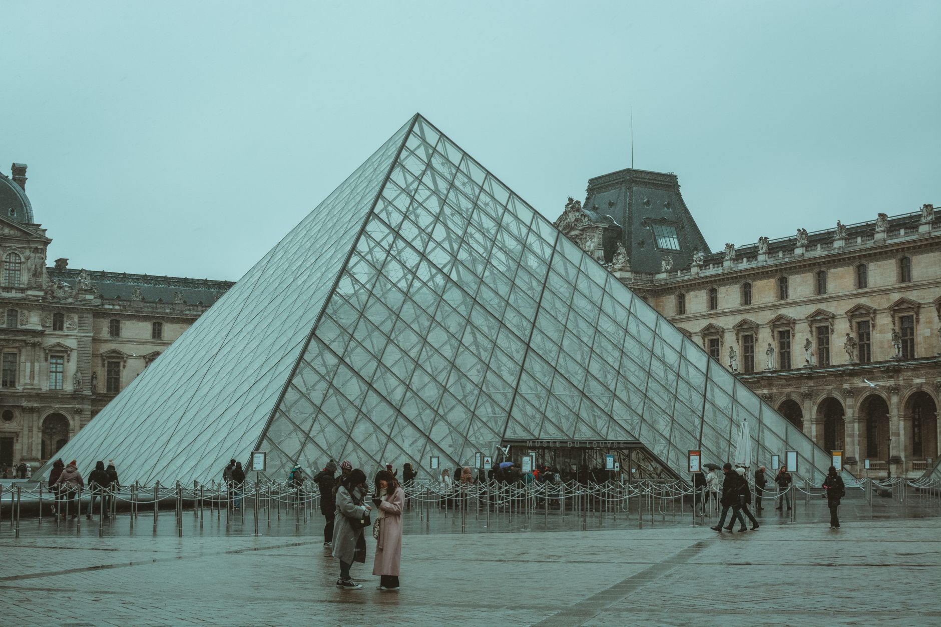 A winter day at the iconic Louvre Museum pyramid in Paris, capturing tourists and the architectural beauty. — Comprehensive G