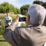 Capture of an outdoor wedding ceremony with an elderly guest taking a photo. — Custom save the dates on your own