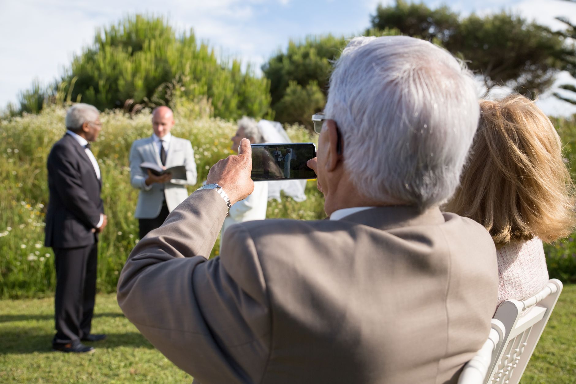 Capture of an outdoor wedding ceremony with an elderly guest taking a photo. — Custom save the dates on your own