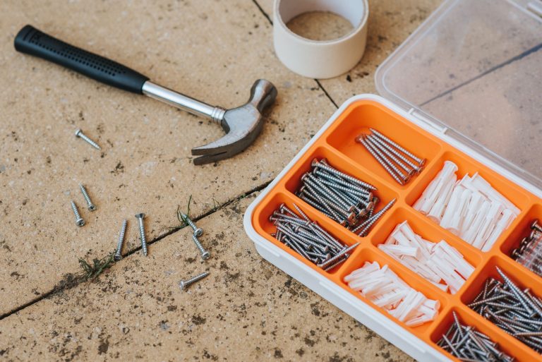 Top view of assorted repair instruments and screws in box near hammer and scotch tape on dirty tile in soft daylight — Differ