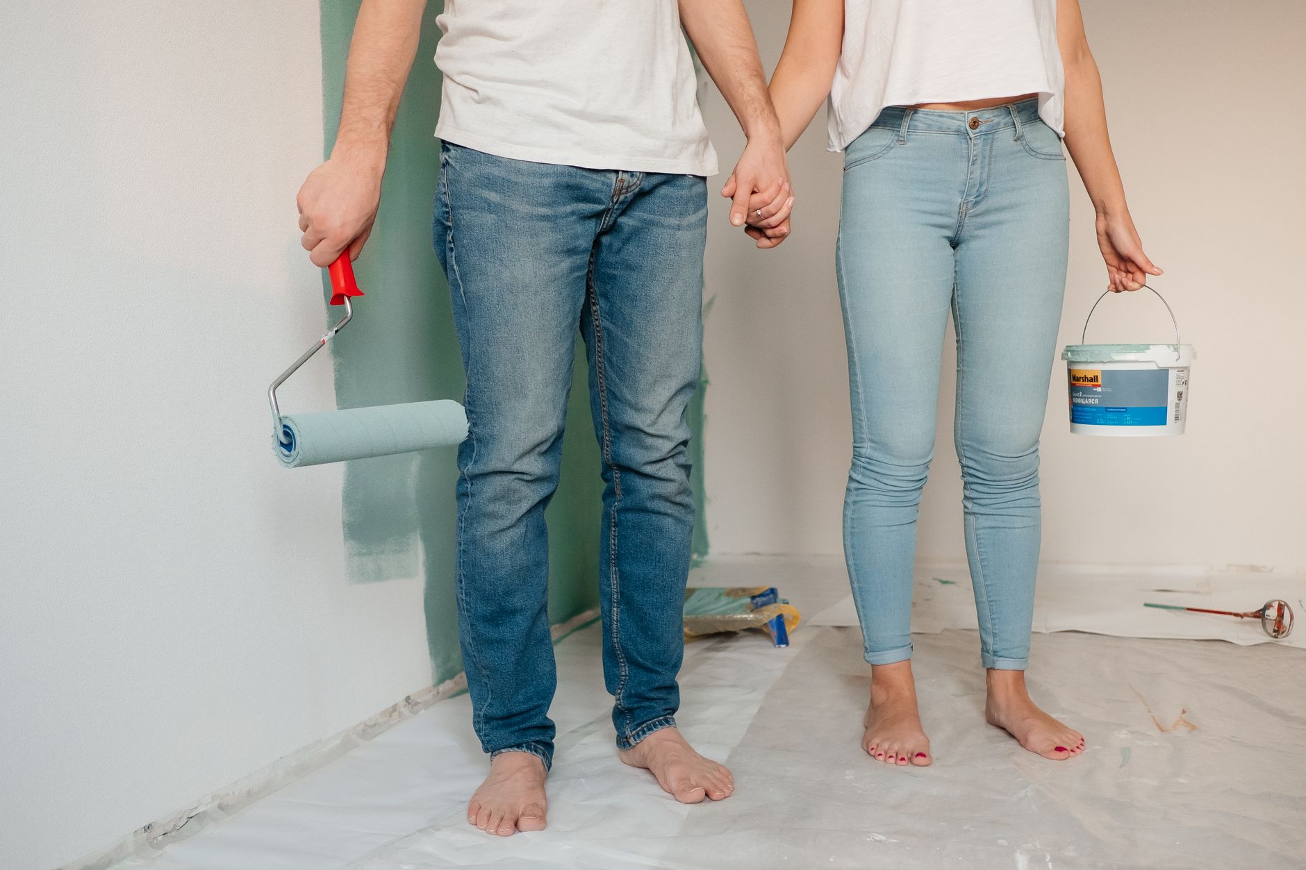 A couple engaged in home renovation, painting a wall barefoot and holding hands, symbolizing love and teamwork. — DO carpets