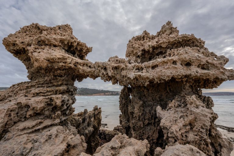 A striking coastal rock formation displaying natural erosion against a cloudy backdrop by the sea. — Download the baazi247 ap