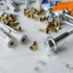 Closeup view of various multicolored plastic dowels with metal screws of different sizes placed on white marble table in mode