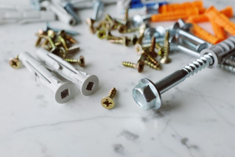 Closeup view of various multicolored plastic dowels with metal screws of different sizes placed on white marble table in mode