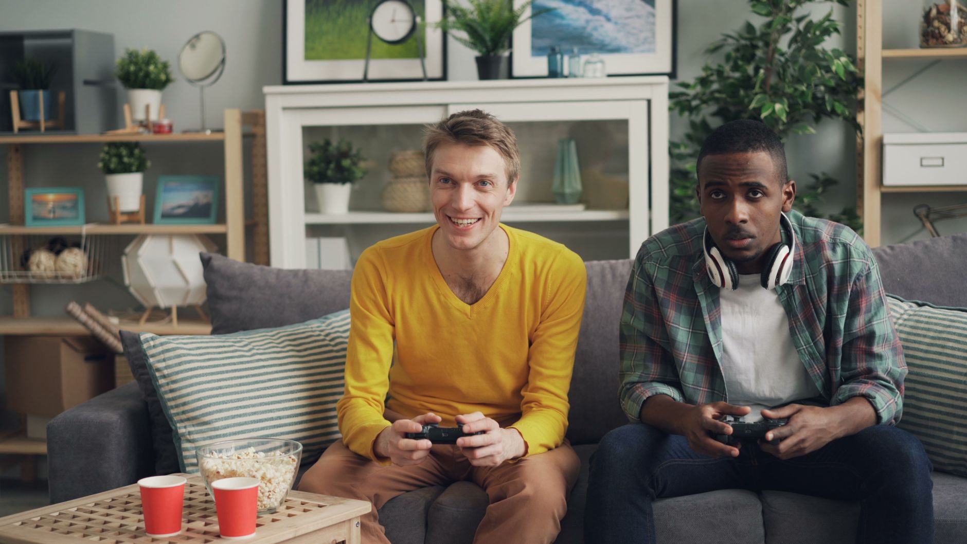 Two friends playing video games together on a sofa, one holding a controller and the other wearing headphones. — Exploring Di