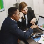 Two business professionals working on growth charts using laptop in an office setting. — FAQs on regular savings plans in Sin