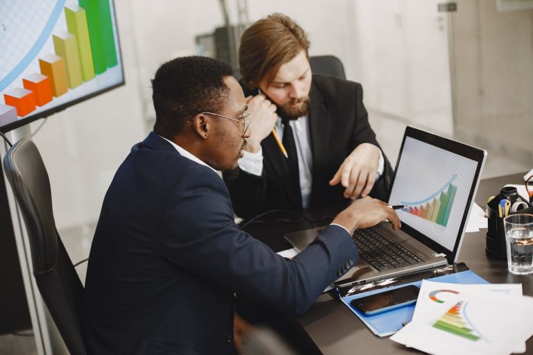 Two business professionals working on growth charts using laptop in an office setting. — FAQs on regular savings plans in Sin