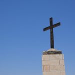 A solitary cross on a stone base stands tall against a vibrant blue sky, symbolizing faith and spirituality. — Few Interestin