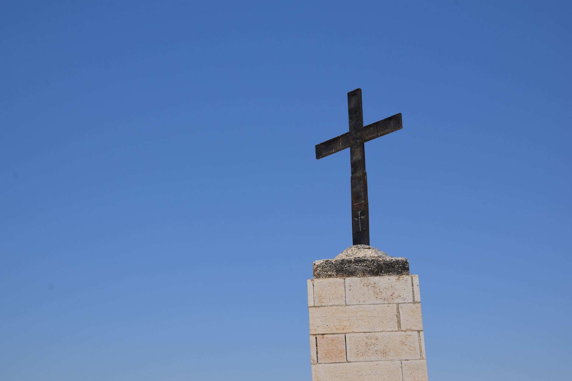 A solitary cross on a stone base stands tall against a vibrant blue sky, symbolizing faith and spirituality. — Few Interestin