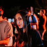 Woman gaming in esports tournament, wearing headset with focused expression, dimmed indoor lighting. — Get To Know The Three