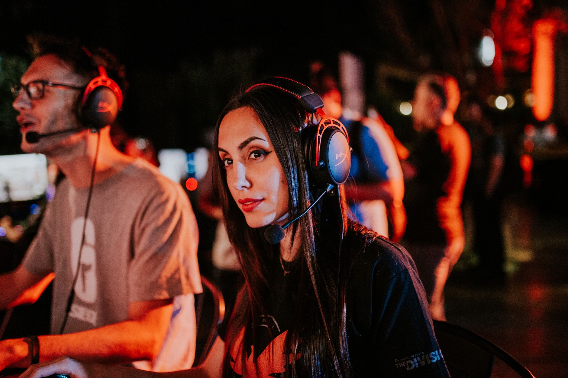 Woman gaming in esports tournament, wearing headset with focused expression, dimmed indoor lighting. — Get To Know The Three