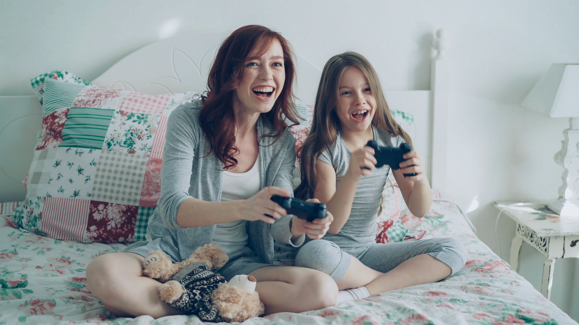 Happy mother and daughter playing video games on bed, enjoying fun family time. — Here Are The Pros And Cons For Undergoing S