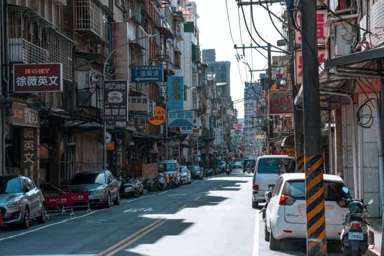 A busy street lined with cars and various colorful business signs on a sunny day. — High-Quality Replica Designer Handbags fo