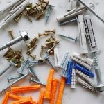 Set of assorted multicolored plastic dowels and various metal screws of different sizes placed on white marble table in works