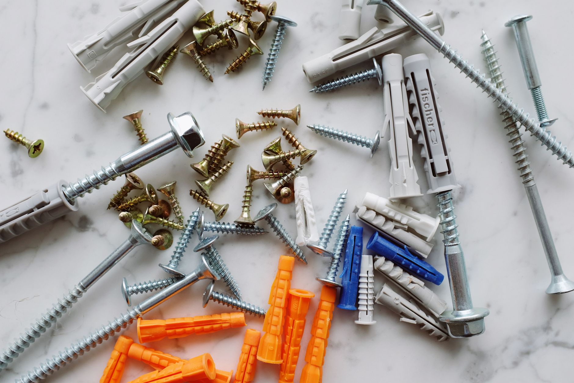 Set of assorted multicolored plastic dowels and various metal screws of different sizes placed on white marble table in works