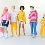 Full body group of positive multiethnic teenager friends with backpack and penny board standing against white wall and lookin