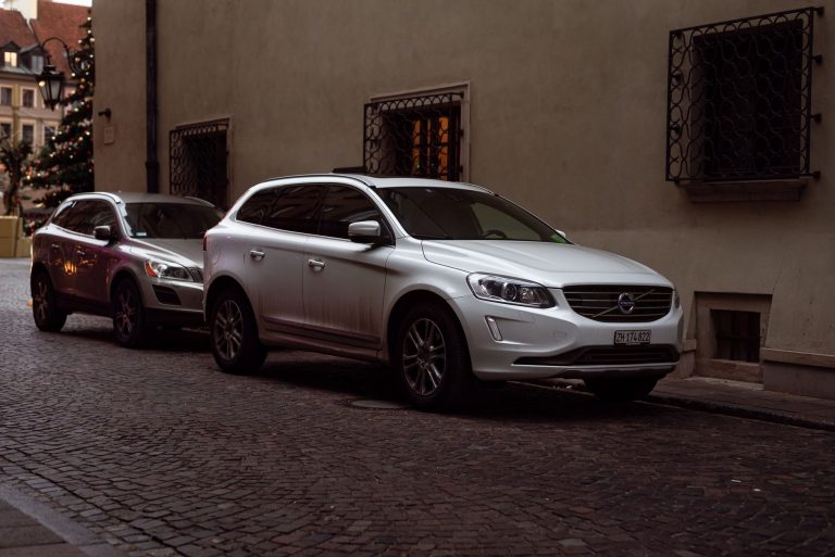 White Volvo SUV parked on cobblestone city street during winter with Christmas decorations. — How to Select a New Garage Door