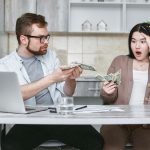 A shocked couple sitting at a table counting cash, illustrating financial surprise. — How VAT Bridging LoansWork And Why You