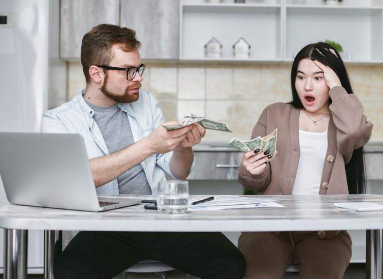 A shocked couple sitting at a table counting cash, illustrating financial surprise. — How VAT Bridging LoansWork And Why You
