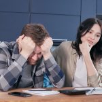 A couple looking worried while reviewing financial documents at a kitchen table. — Importance of Asset Allocation in Retireme