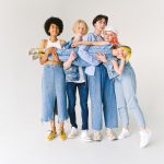 Full body of multiethnic teenagers and schoolchild in casual denim outfit standing in studio and holding kid on hands on whit