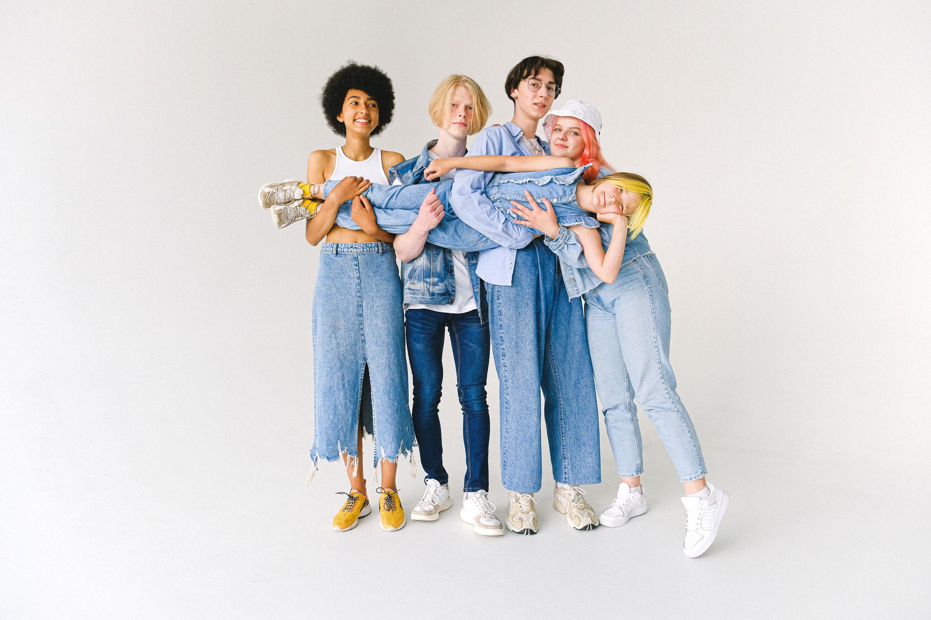 Full body of multiethnic teenagers and schoolchild in casual denim outfit standing in studio and holding kid on hands on whit