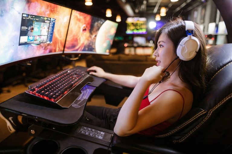 Young woman in red top gaming on dual monitors with white headphones in a modern setup. — Incredible facts that will tend you