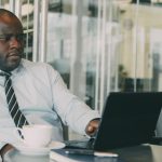 Focused businessman uses laptop in stylish cafe, sipping coffee. Perfect for business or lifestyle themes. — Interventional P