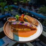 A beautifully plated salmon dish with vegetables and sauce served al fresco, highlighting vibrant culinary presentation. — Is