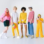 Full body group of informal teenager friends in colorful outfits standing against white background with ball and penny board