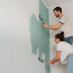 A young couple collaborates on painting a wall with rollers, highlighting teamwork and home improvement. — Is Your Living Roo
