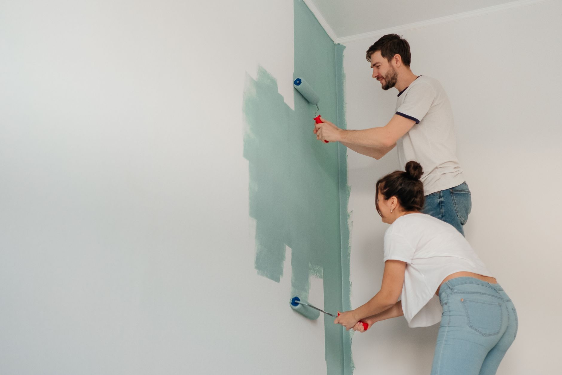 A young couple collaborates on painting a wall with rollers, highlighting teamwork and home improvement. — Is Your Living Roo