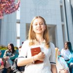 Happy university students socializing on campus, with a focus on a smiling young woman holding a book. — Know More About the