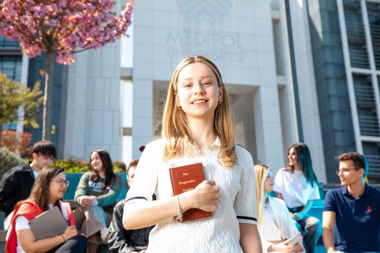 Happy university students socializing on campus, with a focus on a smiling young woman holding a book. — Know More About the