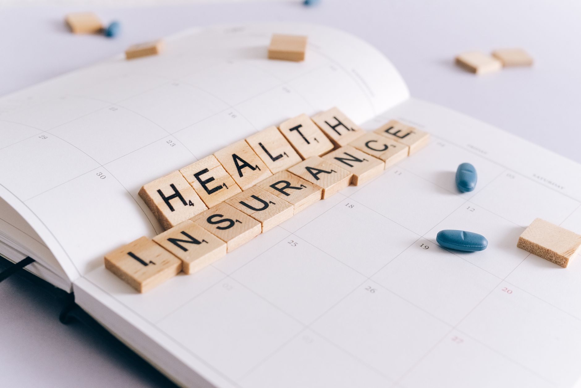 Scrabble tiles spelling 'Health Insurance' on a calendar with pills. — Medicare Advantage Plans and Comparison Methods